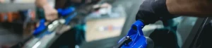 Technicien SOS Pare-Brise+ remplaçant un pare-brise à domicile devant le garage d'un particulier